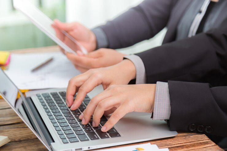 Two people working on ad campaigns: one typing on a computer and the other showing an alternative version on a tablet, illustrating the common mistake of not using A/B testing in Meta Ads.