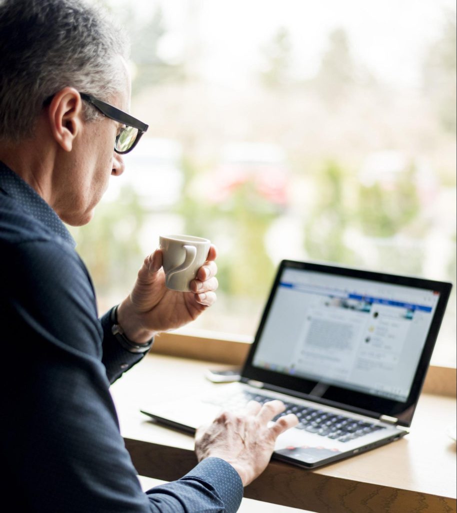 An elderly man using his Facebook on a laptop while holding a cup of coffee, highlighting the common mistake of using a personal profile for Meta Ads