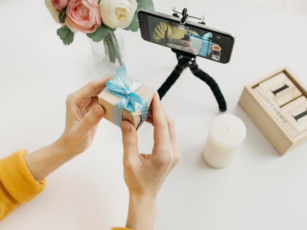 Woman using her phone and a gift box to create social media content for her e-commerce website jewerly store