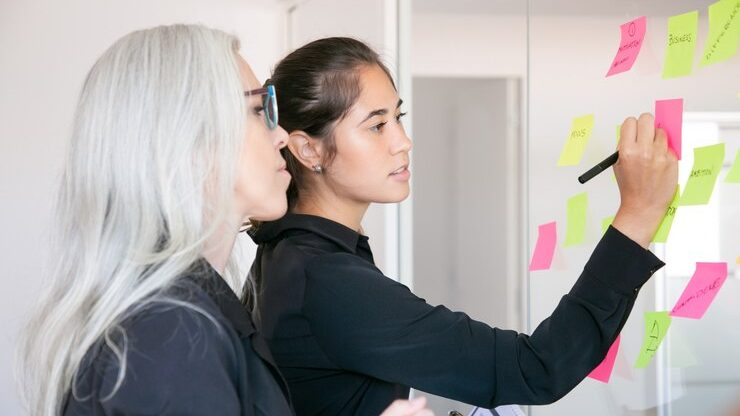 Two women brainstorming with sticky notes on a glass board, representing innovative marketing trends for 2025.