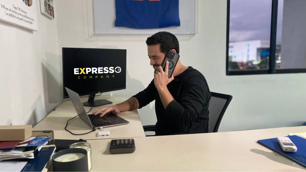 Federico Chamorro, CEO of Expresso Company, working at his desk with a phone in hand and a laptop, demonstrating the benefits of outsourcing for small businesses in a professional work environment.
