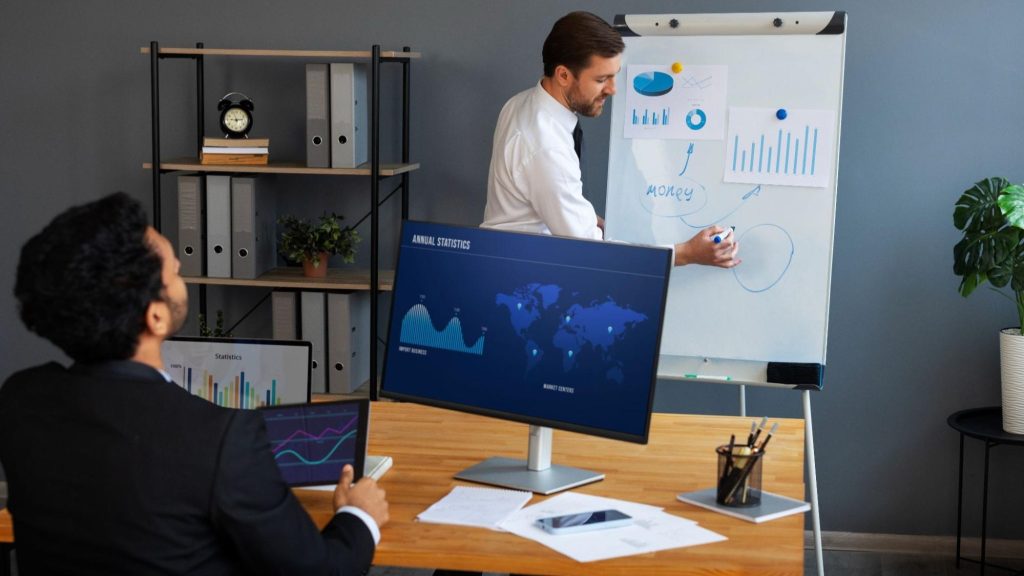 A presenter explaining data-driven strategies with a whiteboard and digital screens, showcasing predictive analytics and ROI in marketing.