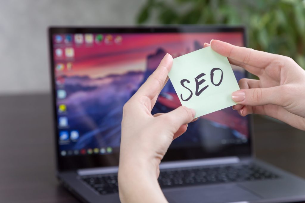 Sticky note labeled SEO in front of a laptop used for AI search strategy